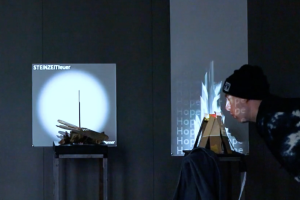 In zwei Installationen werden analoge Objekte mitteles einer Projektion an der Wand augmentiert. Ein Mensch interagiert mit einer der Installationen in dem er in einen Holzhaufen pustet. In der Projektion wird ein Feuer angefacht.  