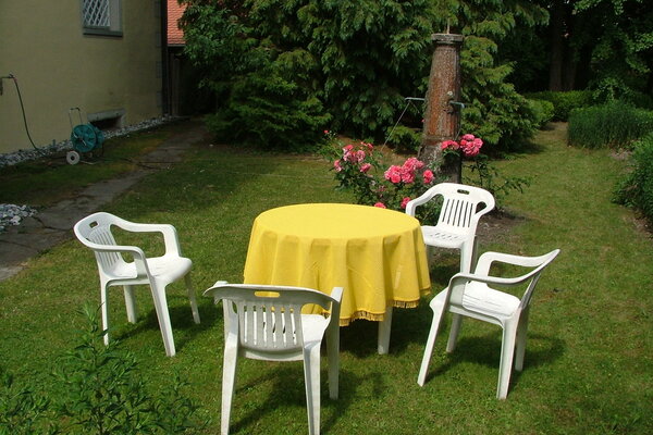 In einem Garten stehen vier Monobloc-Plastikstühle um einen mit einer gelben Tischdecke bedeckten Plastiktisch.