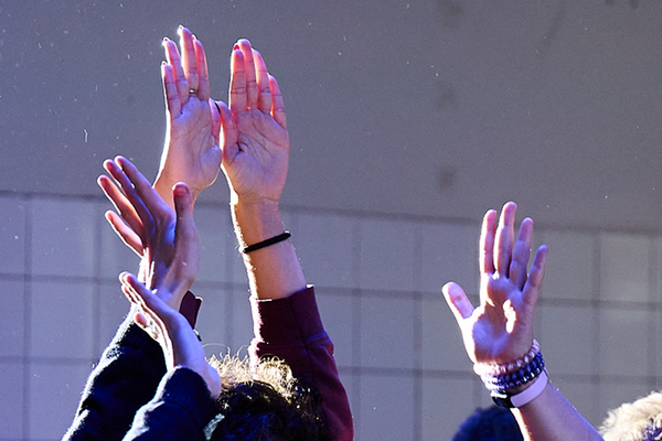  A photo of three people in a studio raising their hands into the air. Light meets fingerstips, dust particles dance. What can’t be seen in the photo is that the people are touching an imaginary object that tingles between their hands.